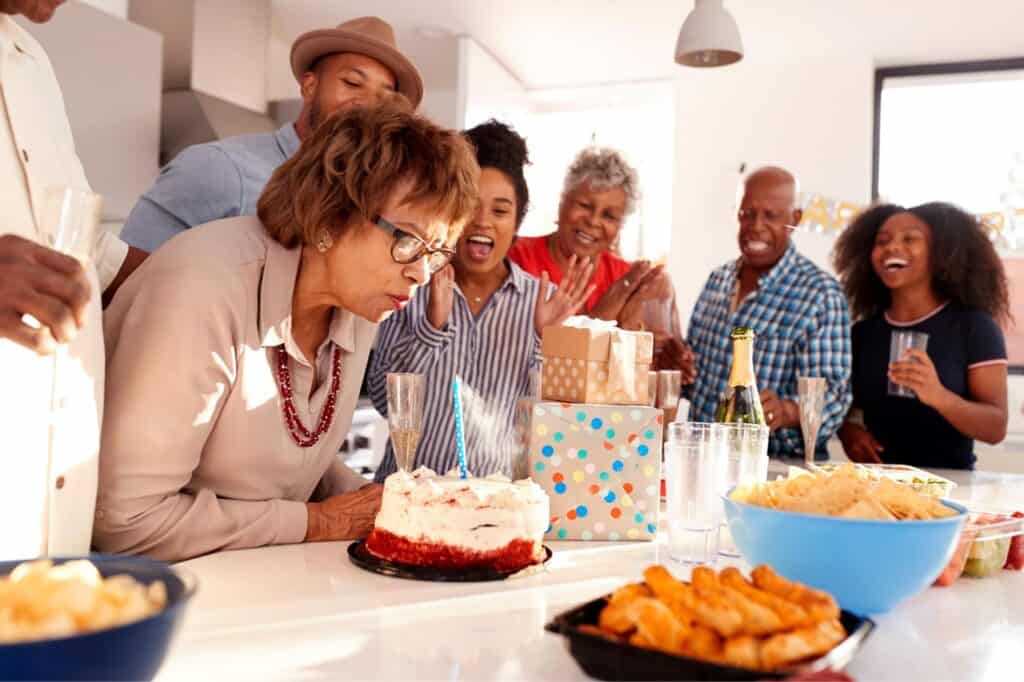 Group of diverse seniors celebrating with cake and friends, embracing gray hair confidence.