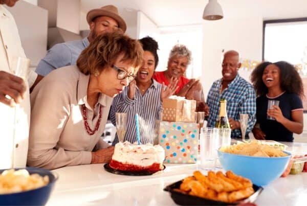 Group of diverse seniors celebrating with cake and friends, embracing gray hair confidence.