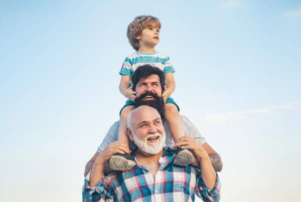 Happy older man with gray hair and a young boy on his shoulders outdoors.