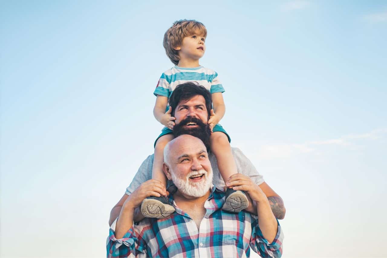 Happy older man with gray hair and a young boy on his shoulders outdoors.