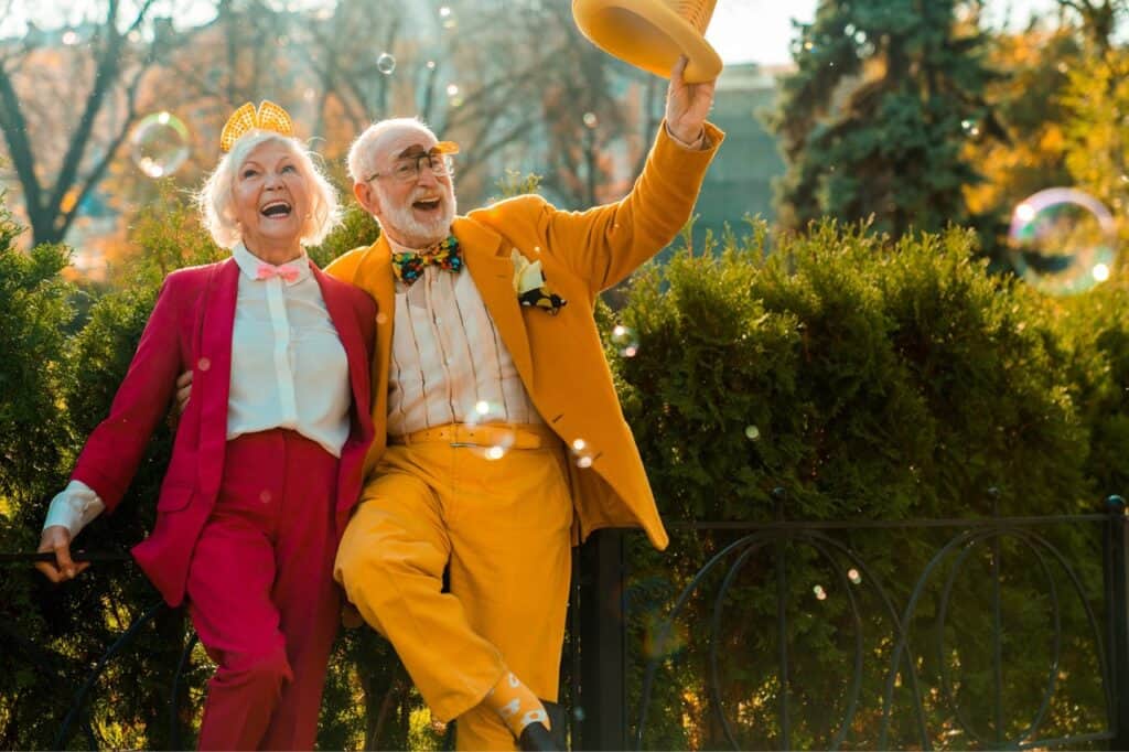Older couple enjoying a joyful moment in the park with colorful outfits and playful bubbles.