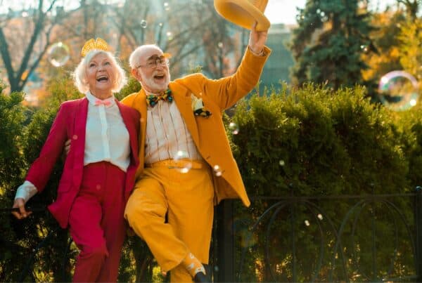 Older couple enjoying a joyful moment in the park with colorful outfits and playful bubbles.