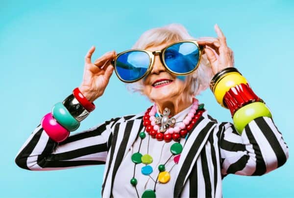 Senior woman with gray hair wearing colorful accessories and sunglasses.