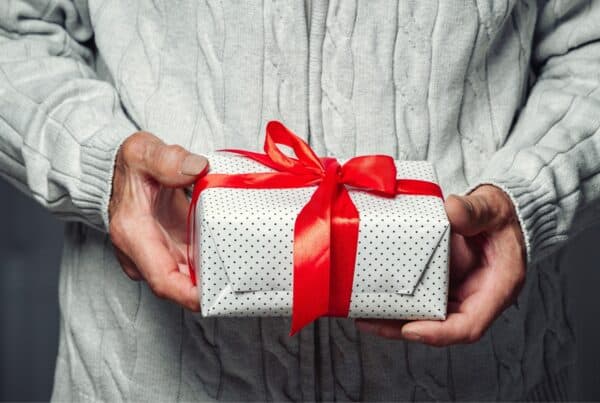 Person holding a wrapped gift with red ribbon, celebrating gray hair confidence.