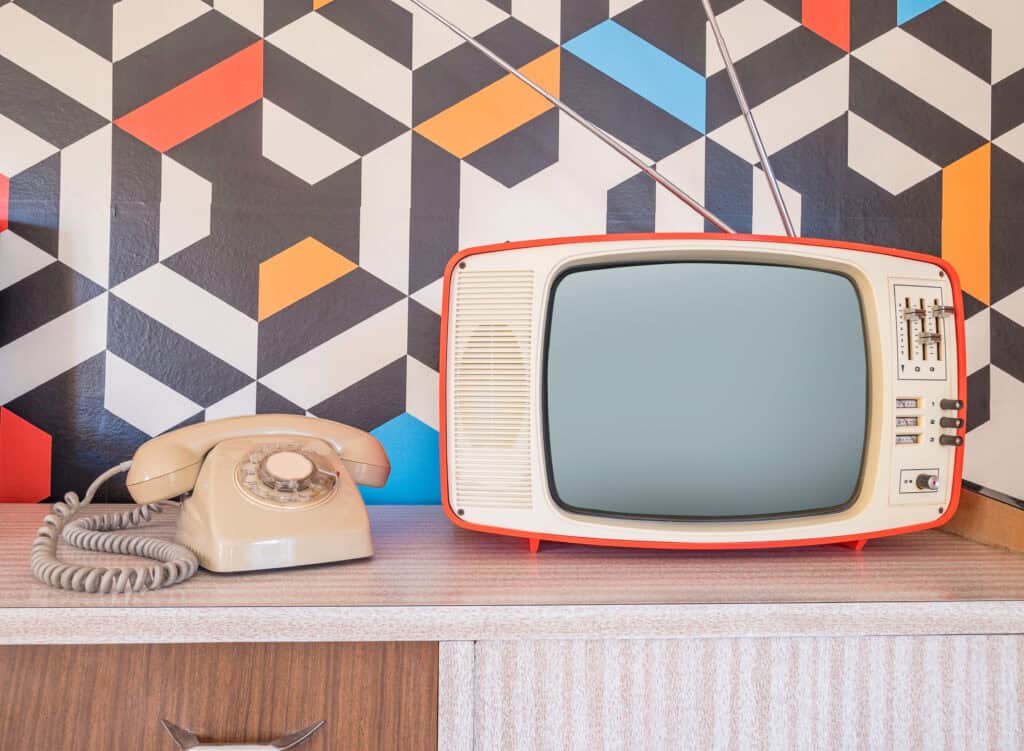 Vintage TV and rotary phone on wooden surface with geometric wall background.