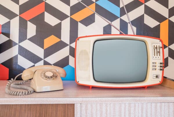Vintage TV and rotary phone on wooden surface with geometric wall background.
