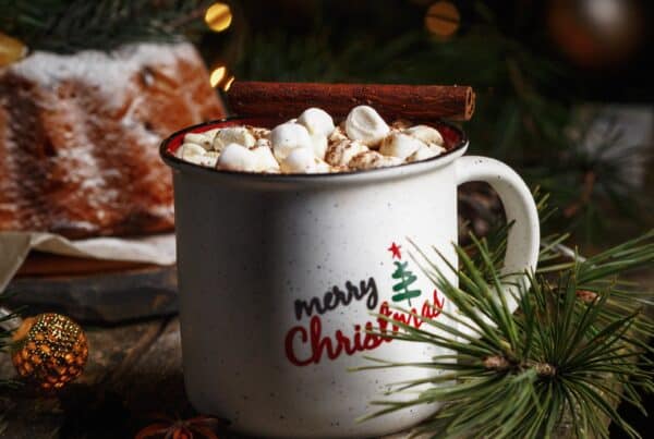 Festive mug with marshmallows and cinnamon stick, holiday decor background.