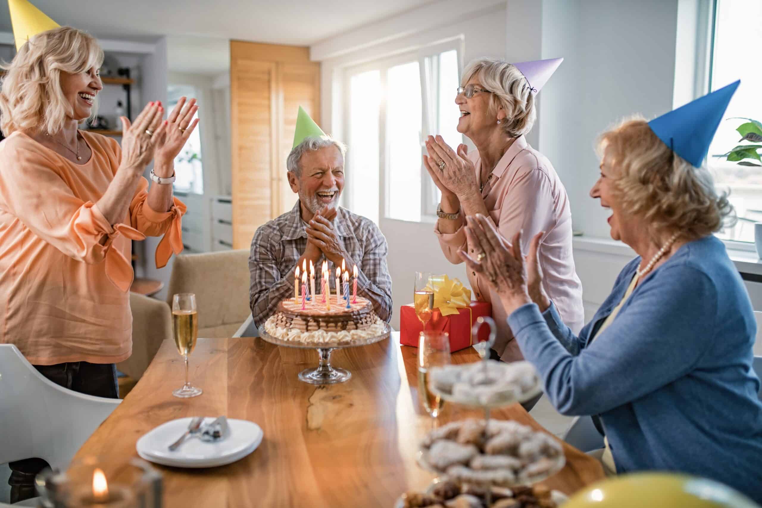 Senior women celebrating birthday with gray hair, party hats, and cake.