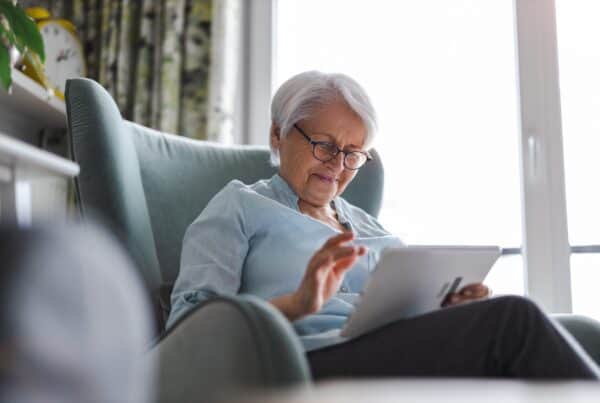 Senior woman with gray hair reading tablet at home, embracing natural hair.