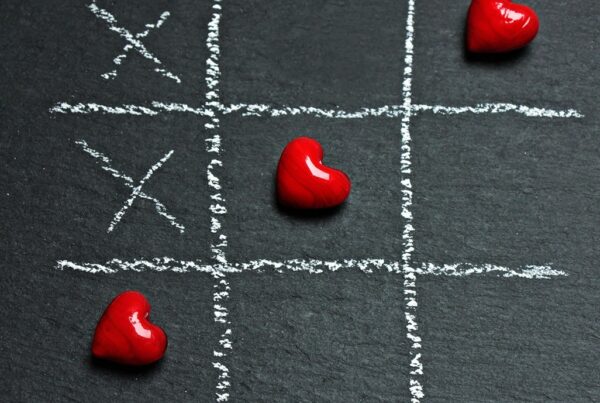 Tic-tac-toe game with red hearts on a chalkboard background, symbolizing love and connection.