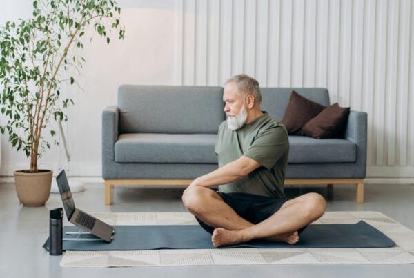 Older man practicing yoga at home with gray hair, promoting wellness for seniors.