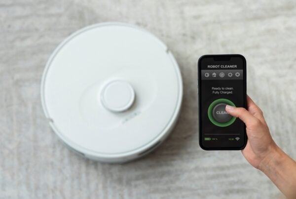 Person controlling a robot vacuum with a smartphone for easy home cleaning.